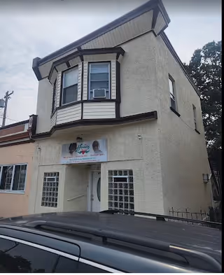 Two-story beige building with bay window and a Healing Hands Helps sign above the entrance.