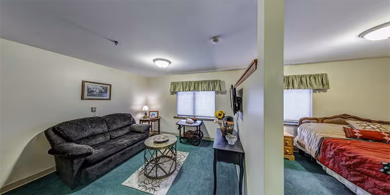 Interior of a senior living suite with living area couch, TV, and bedroom.