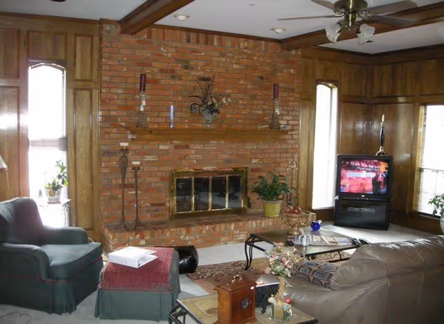 Cozy living room with brick fireplace, wood paneling, and sofa seating around a coffee table.