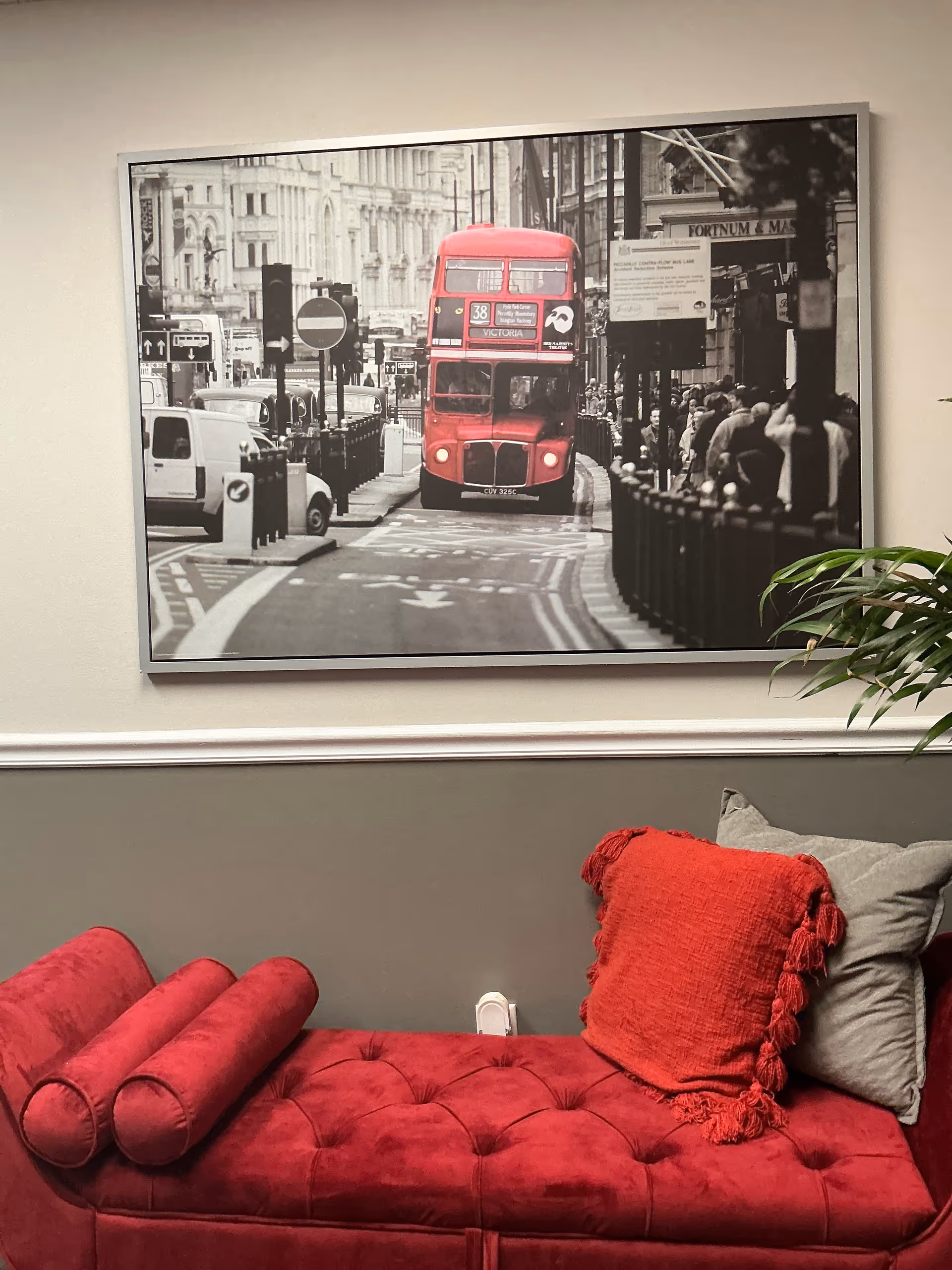 Red velvet sofa with cushions in front of a framed black-and-white city street photograph.