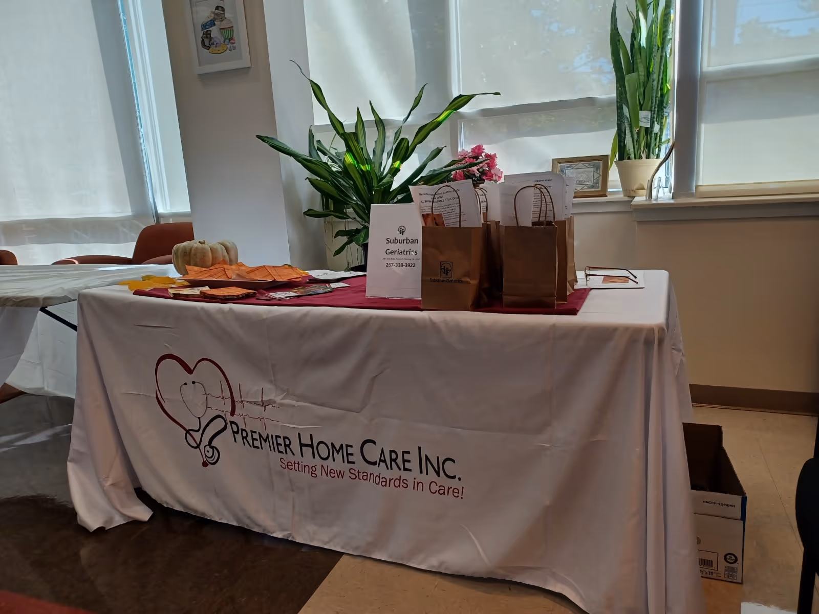 Indoor event table with Premier Home Care Inc. banner, gift bags, and plants.