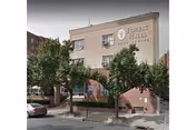 Three-story beige building labeled Forest Hills Care Center, with trees and parked cars nearby.