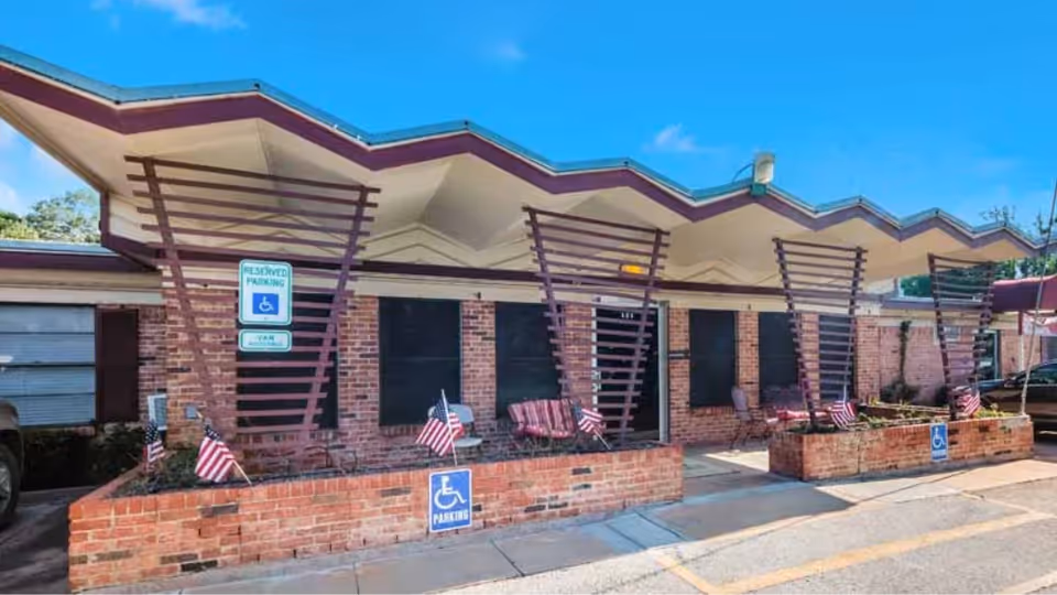 Front exterior of Retama Manor Nursing Center with brick walls, angled canopies, and small planters.