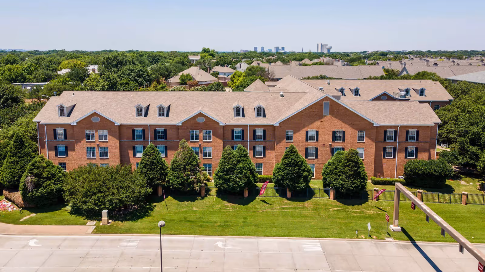 Brick senior living building with manicured lawn and trees, viewed from the street.