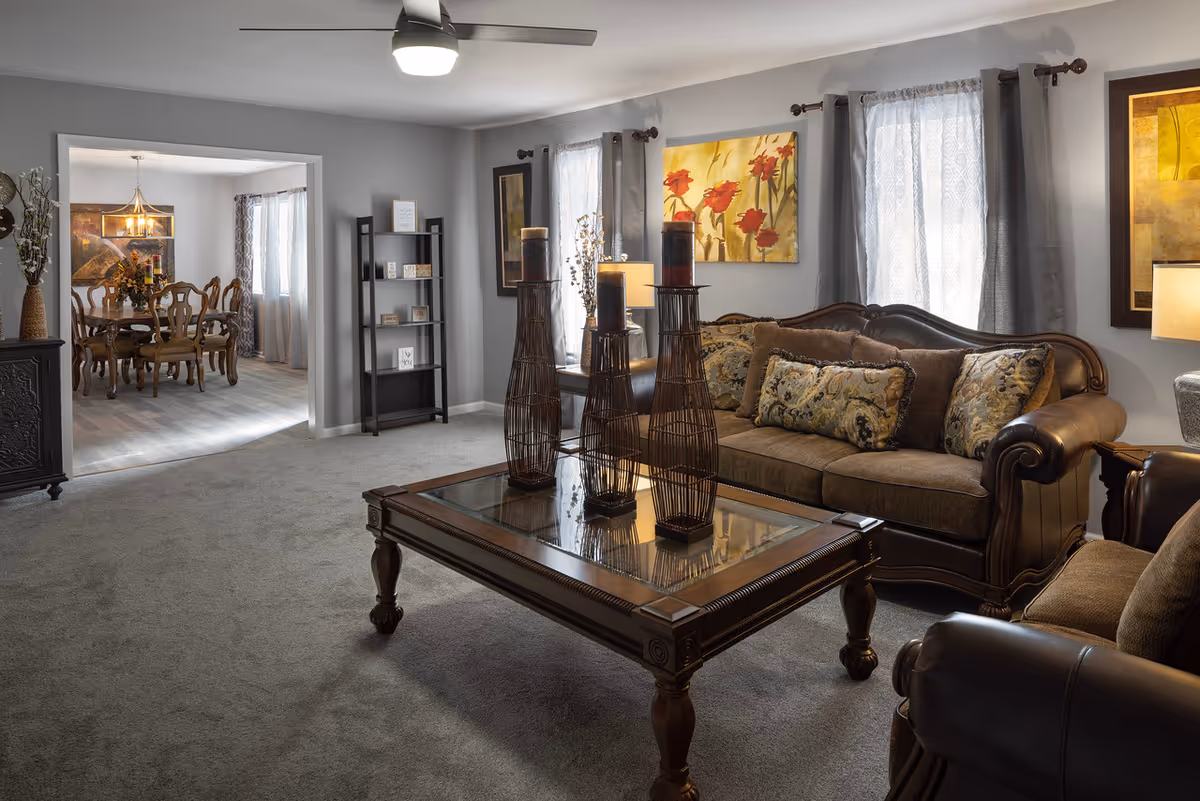 Cozy senior living room with a brown leather sofa, matching chairs, and a glass coffee table.