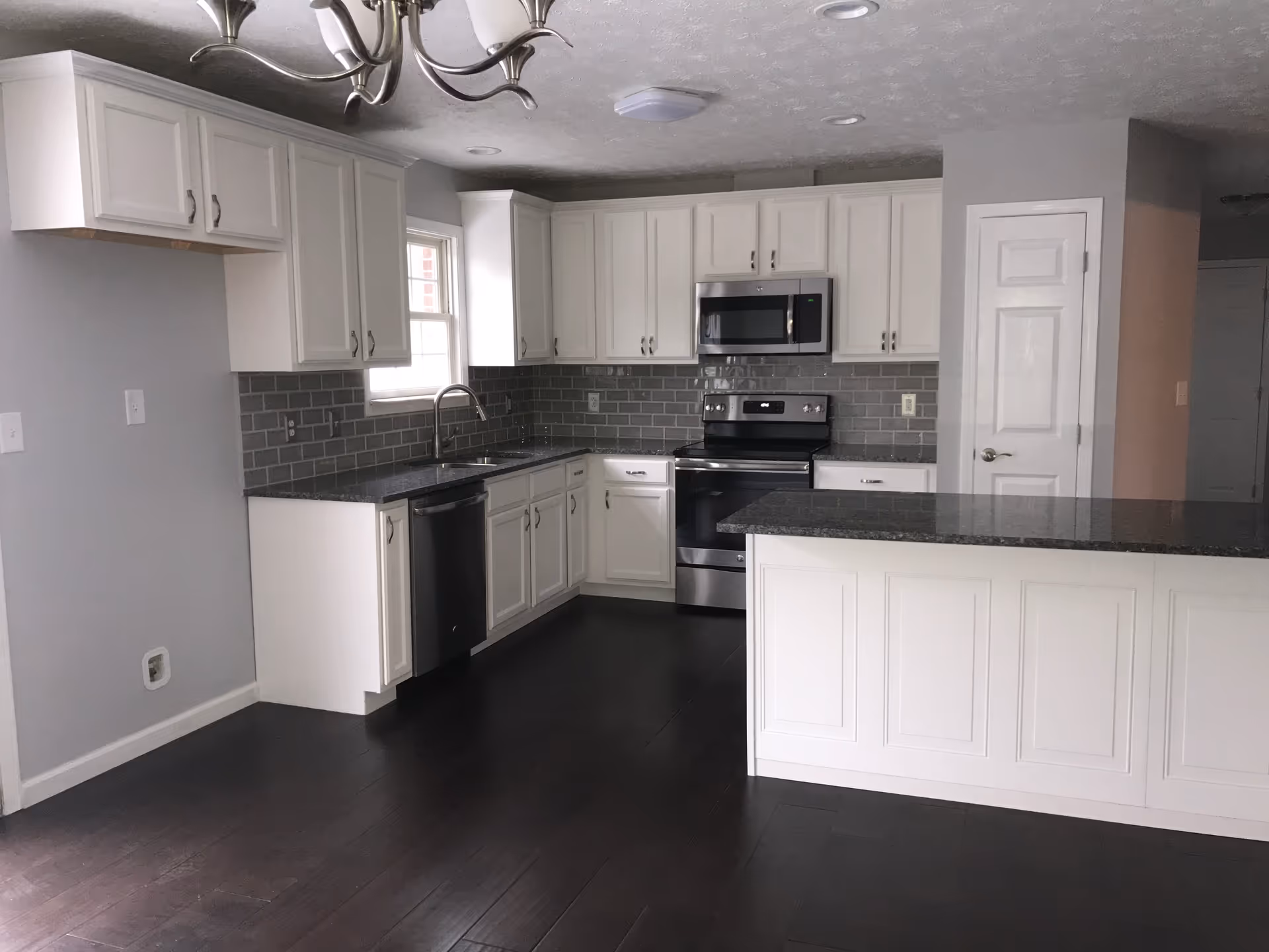 Modern white kitchen with gray backsplash, dark countertops, and stainless steel appliances.