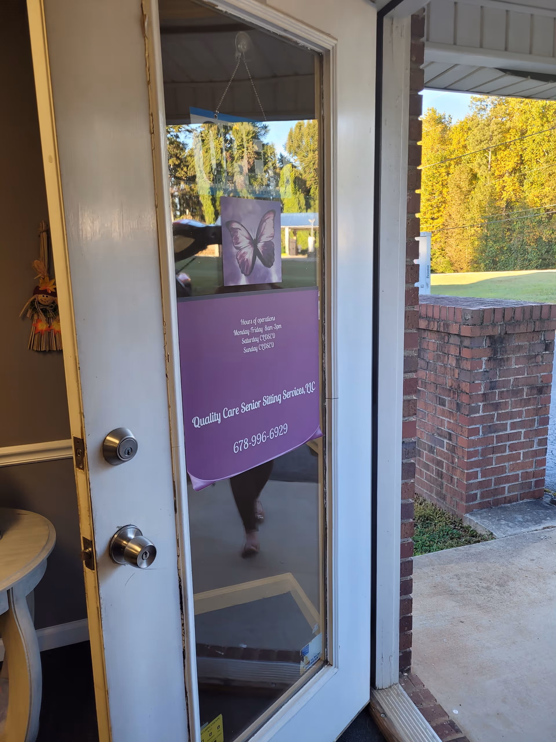Open glass door to senior living facility with purple banner; brick exterior visible.