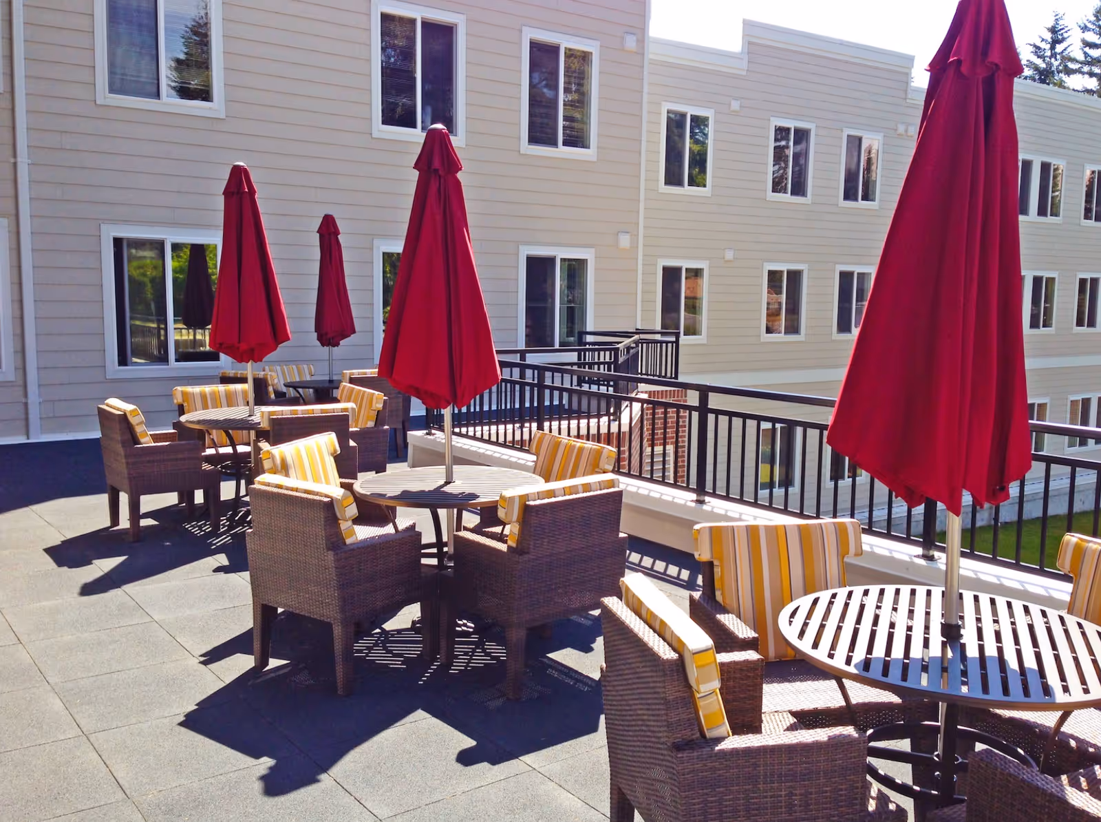 Outdoor terrace with wicker seating, red umbrellas, and a multi-story building backdrop.