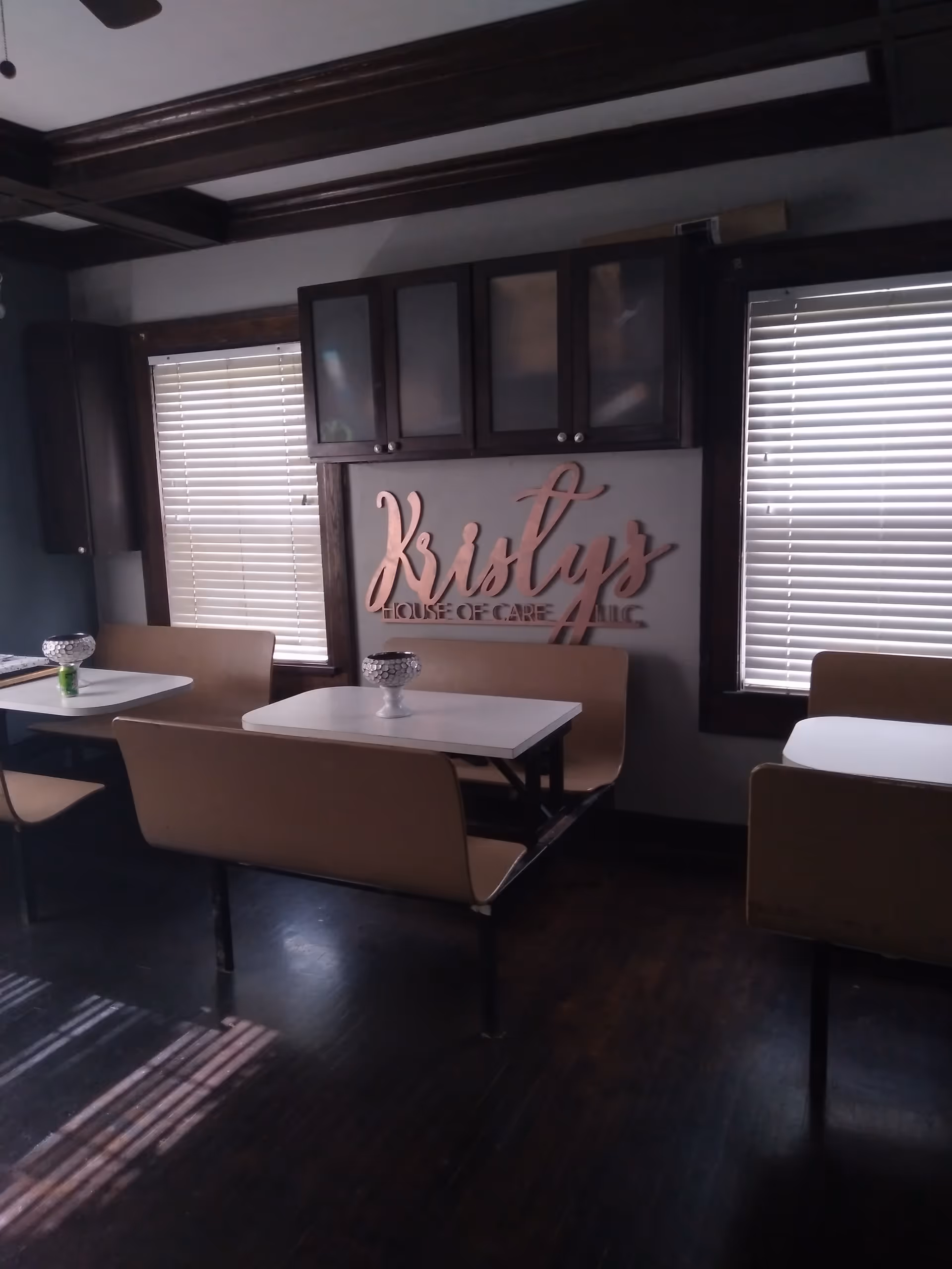 Dining area with booth seating, white tables, blinds, and a Kristy's House of Care sign.