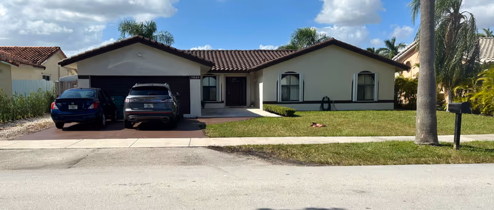 Front view of a single-story facility with two cars parked in driveway and palm trees.