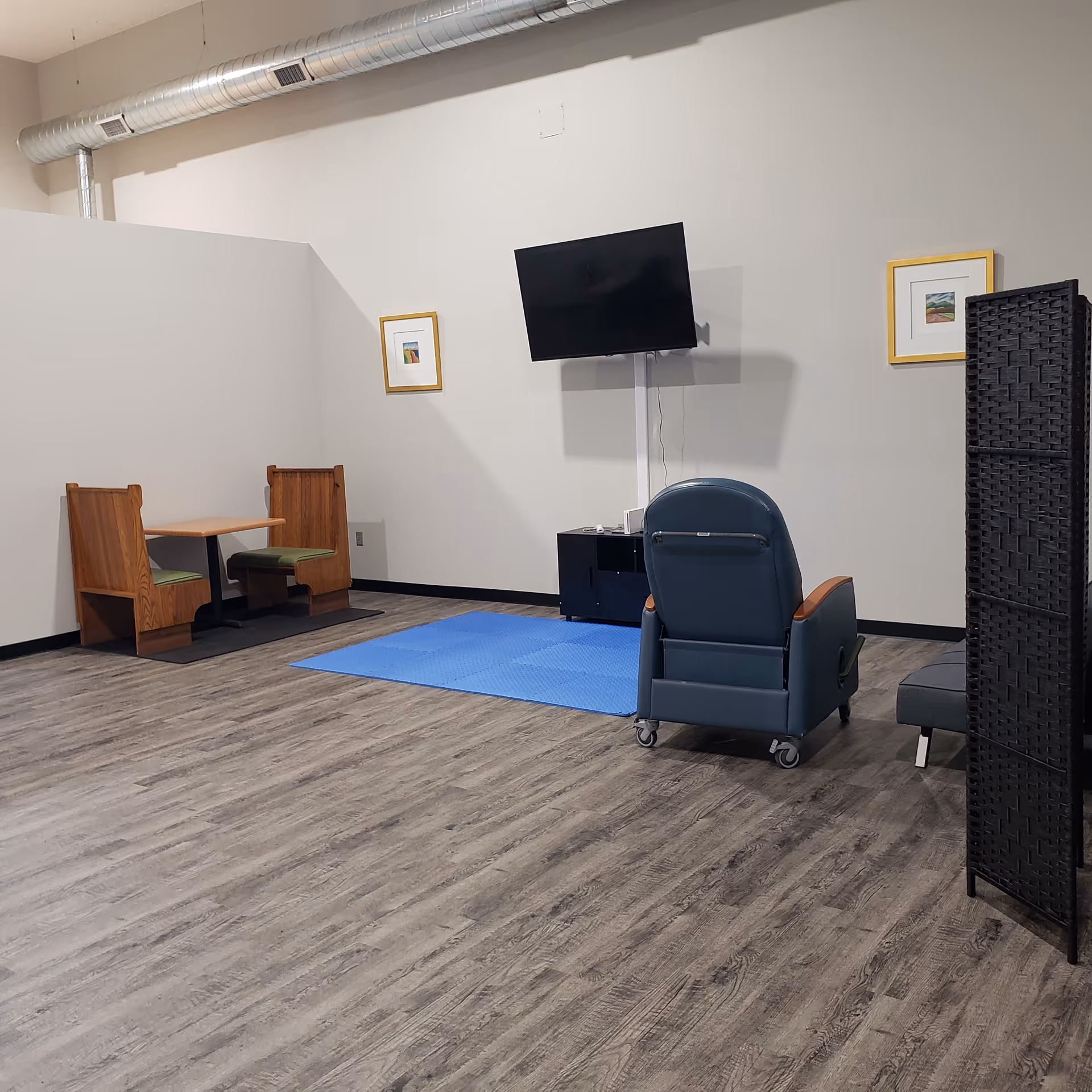 A common lounge area with a mounted TV, recliner chair, blue mat, and seating.