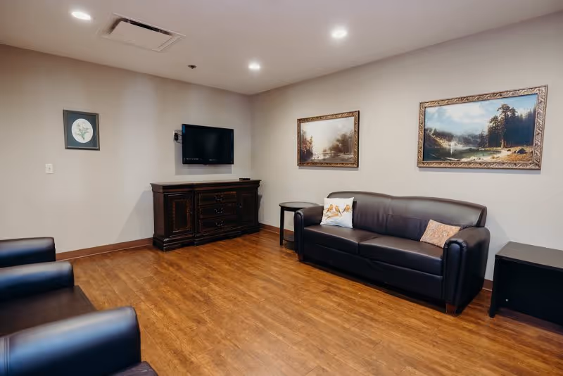 A spacious lounge with leather sofa, chairs, a TV, paintings, and wooden flooring.