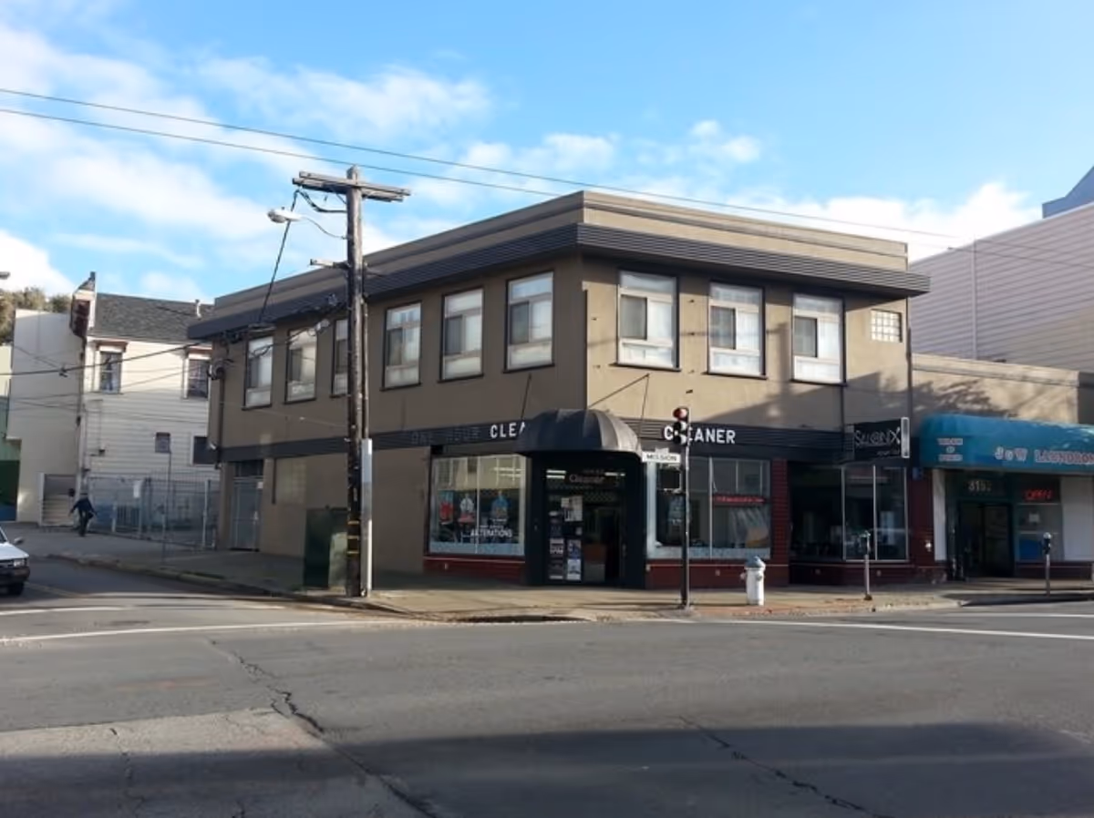 Two-story brick commercial building on a street corner with storefronts and a cloudy sky.