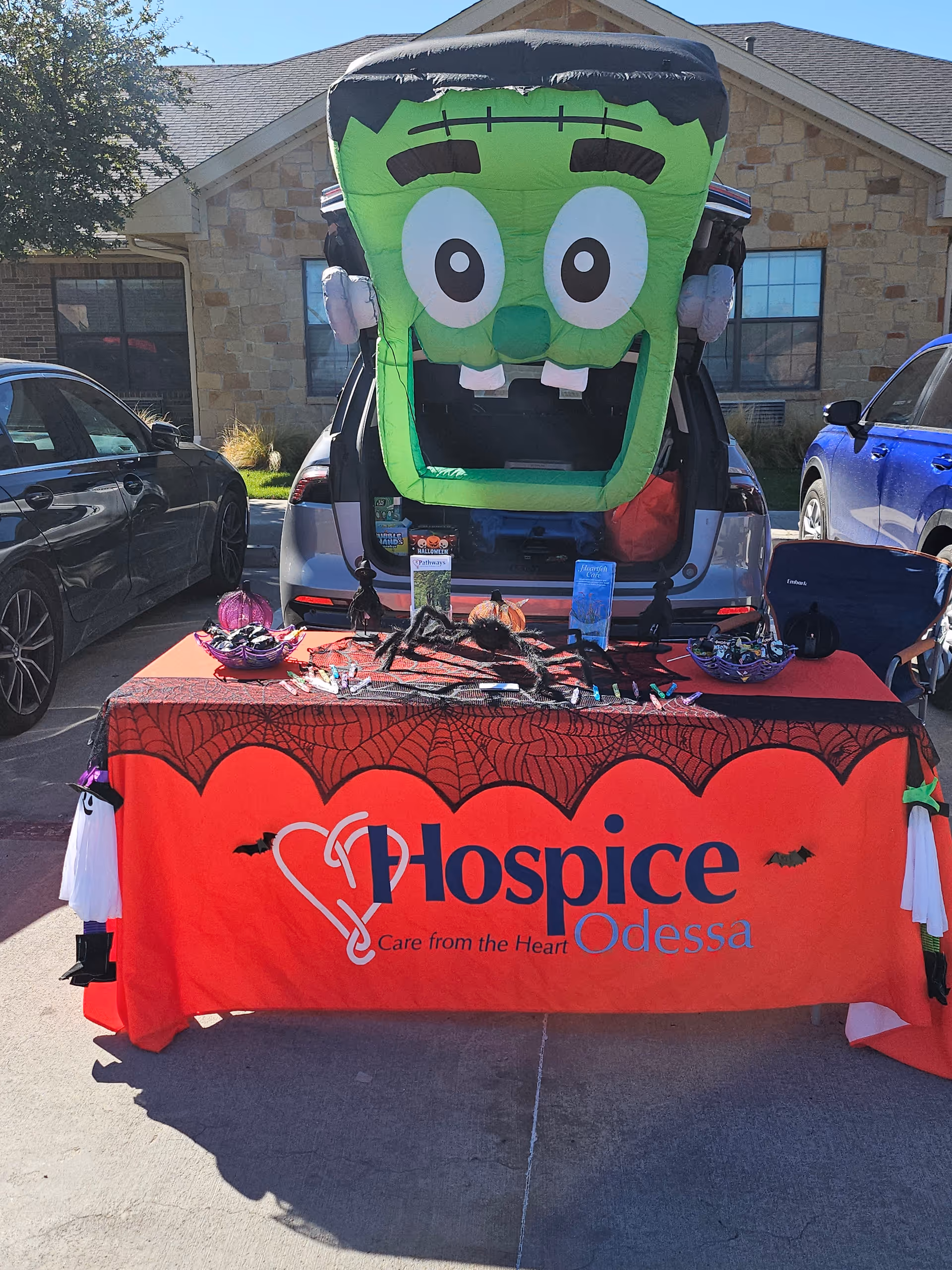 Outdoor charity table with a large Frankenstein balloon and Hospice Odessa banner in a parking lot
