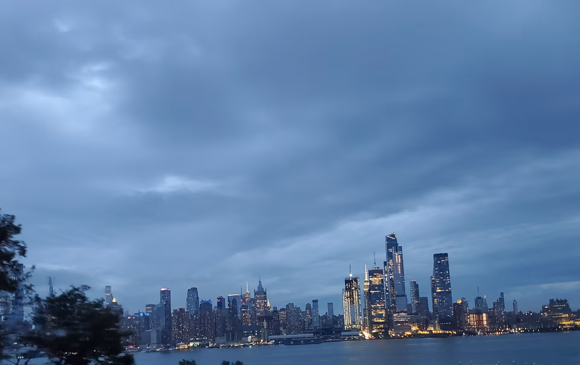 City skyline across a river at dusk with illuminated skyscrapers.