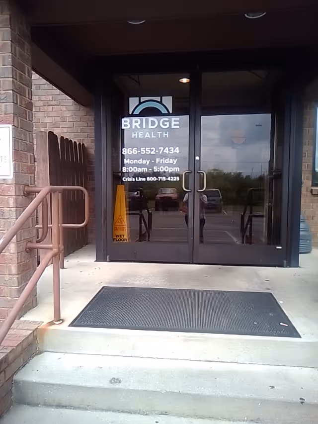 Exterior view of Bridge Health entrance with glass doors, railing, and a wet floor sign.