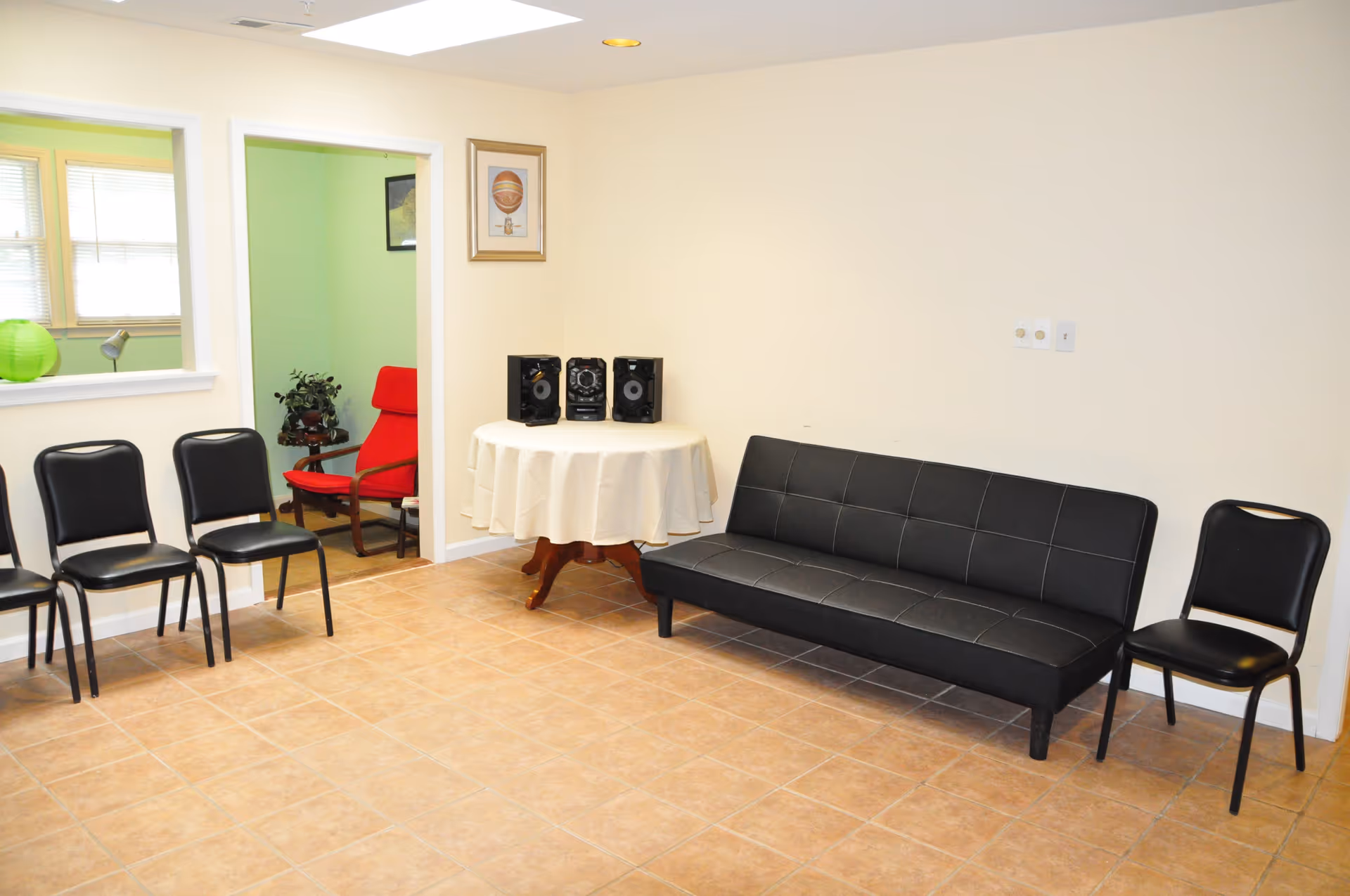 Beige-walled lounge in a senior living facility with black seating and a round table.