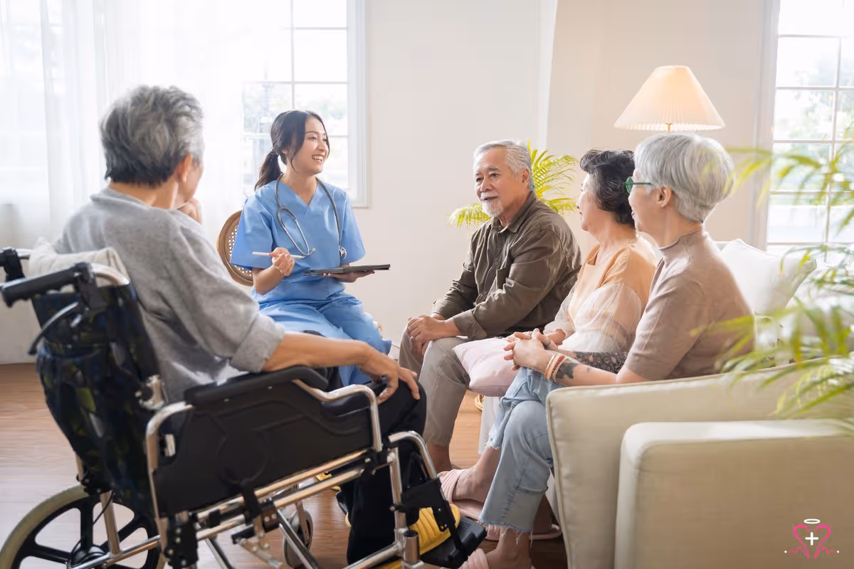Caregiver in blue scrubs chats with seniors in a bright living room.