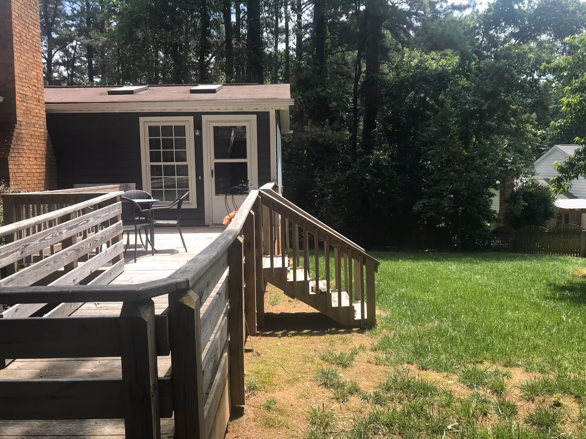 Outdoor wooden deck with seating attached to a brick building and grassy yard.