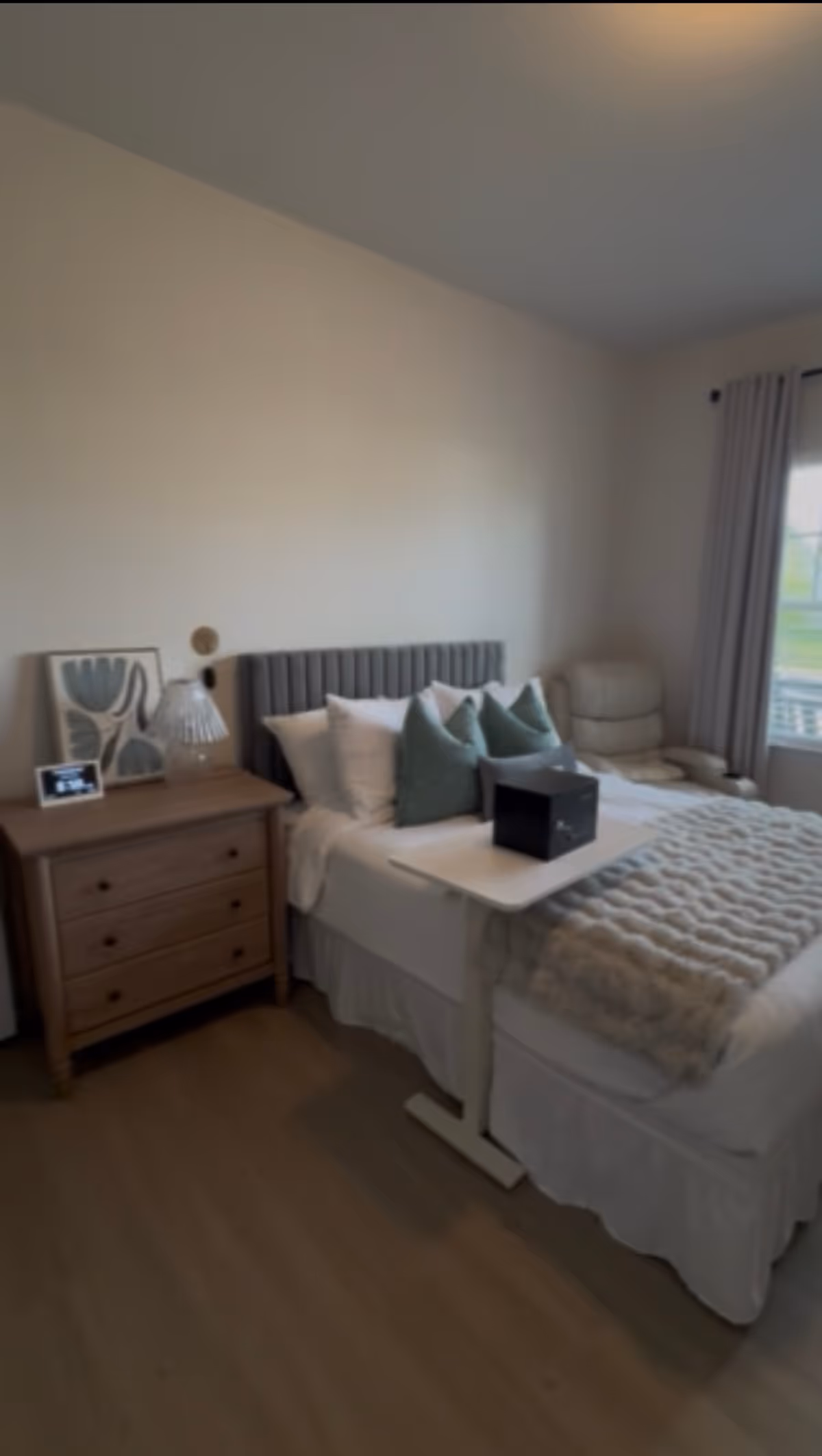 A tidy bedroom with a bed, dresser, and window-side chair.