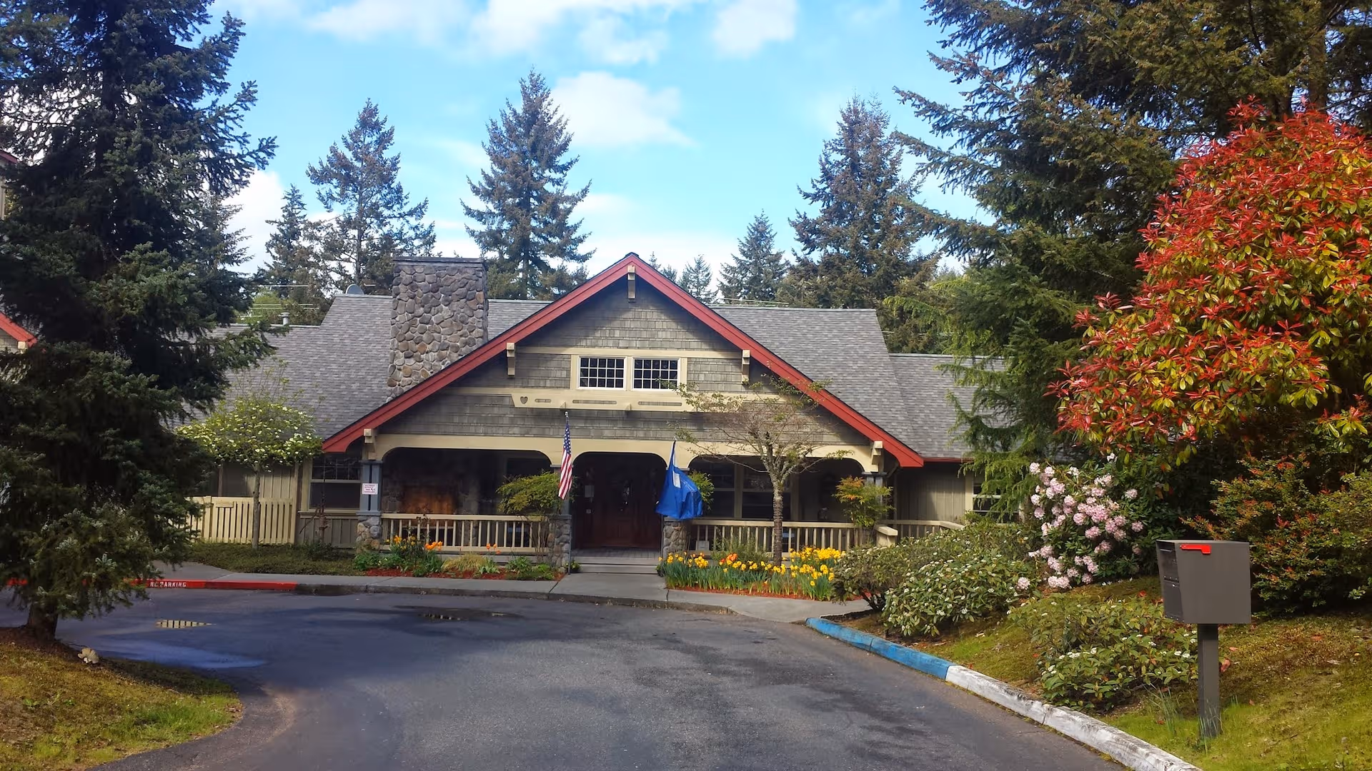 Front view of Greenlake Senior Living building with porch, garden, and surrounding trees.