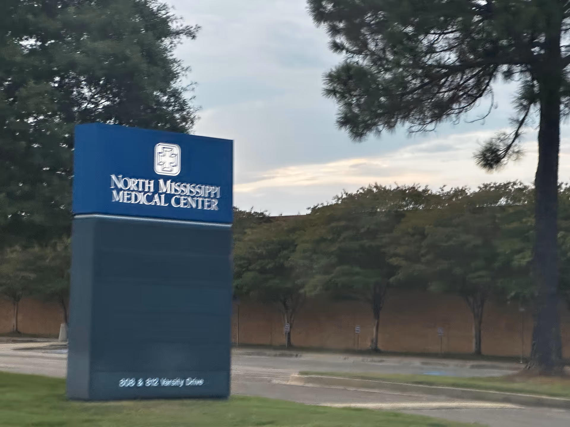Blue North Mississippi Medical Center sign in front of trees and parking area.