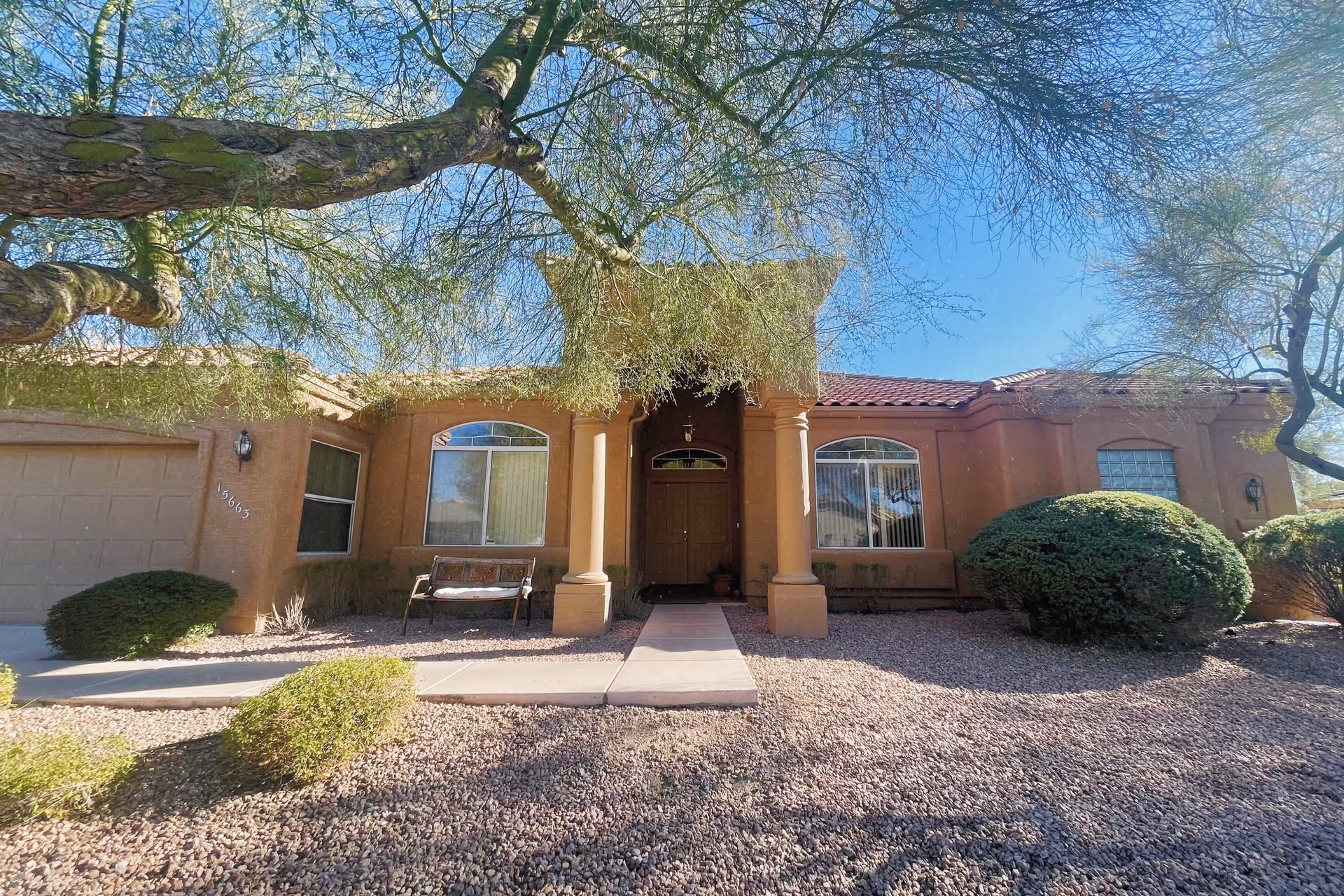 Front view of Fountainview Assisted Living Home with tan stucco, columns, and desert landscaping