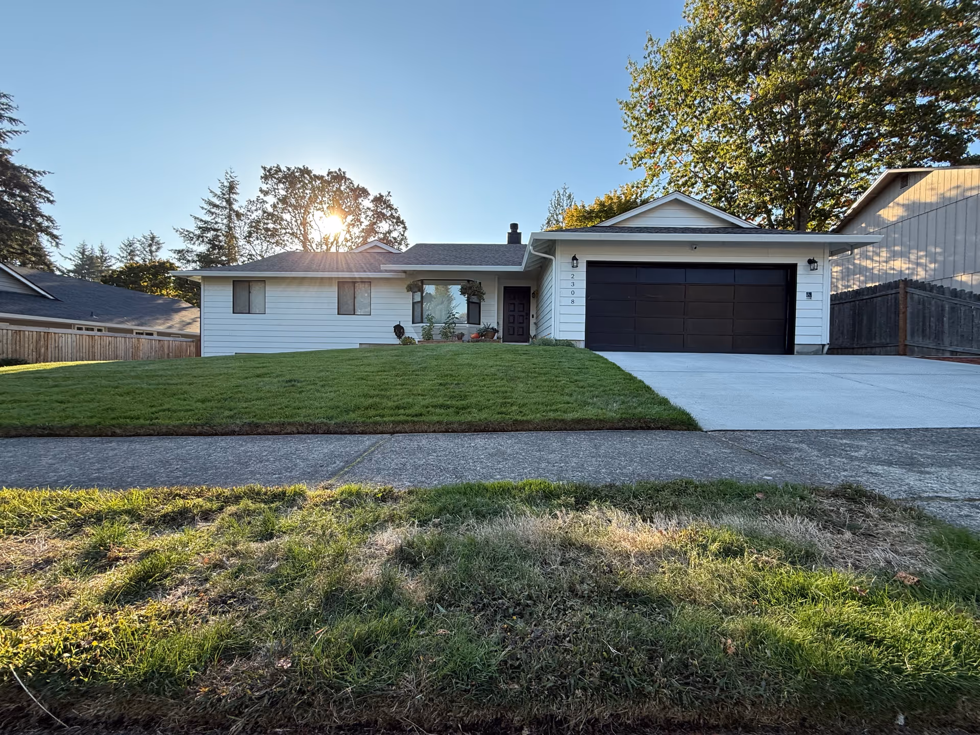White, single-story home with a black garage door, green lawn, and concrete driveway.