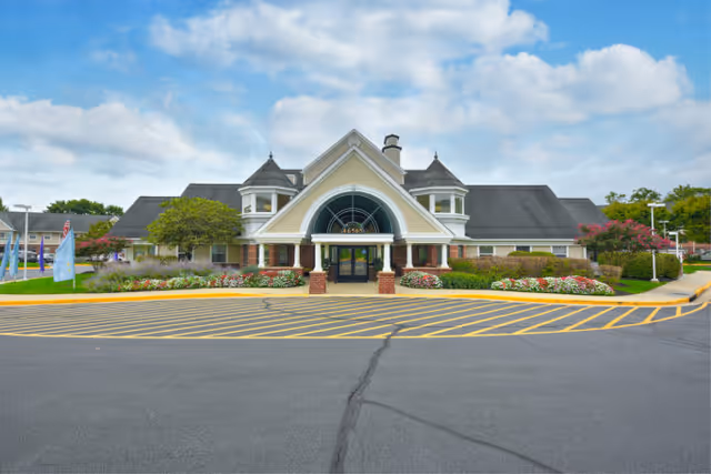 Front view of a senior living facility with a curved glass entrance and landscaped front.