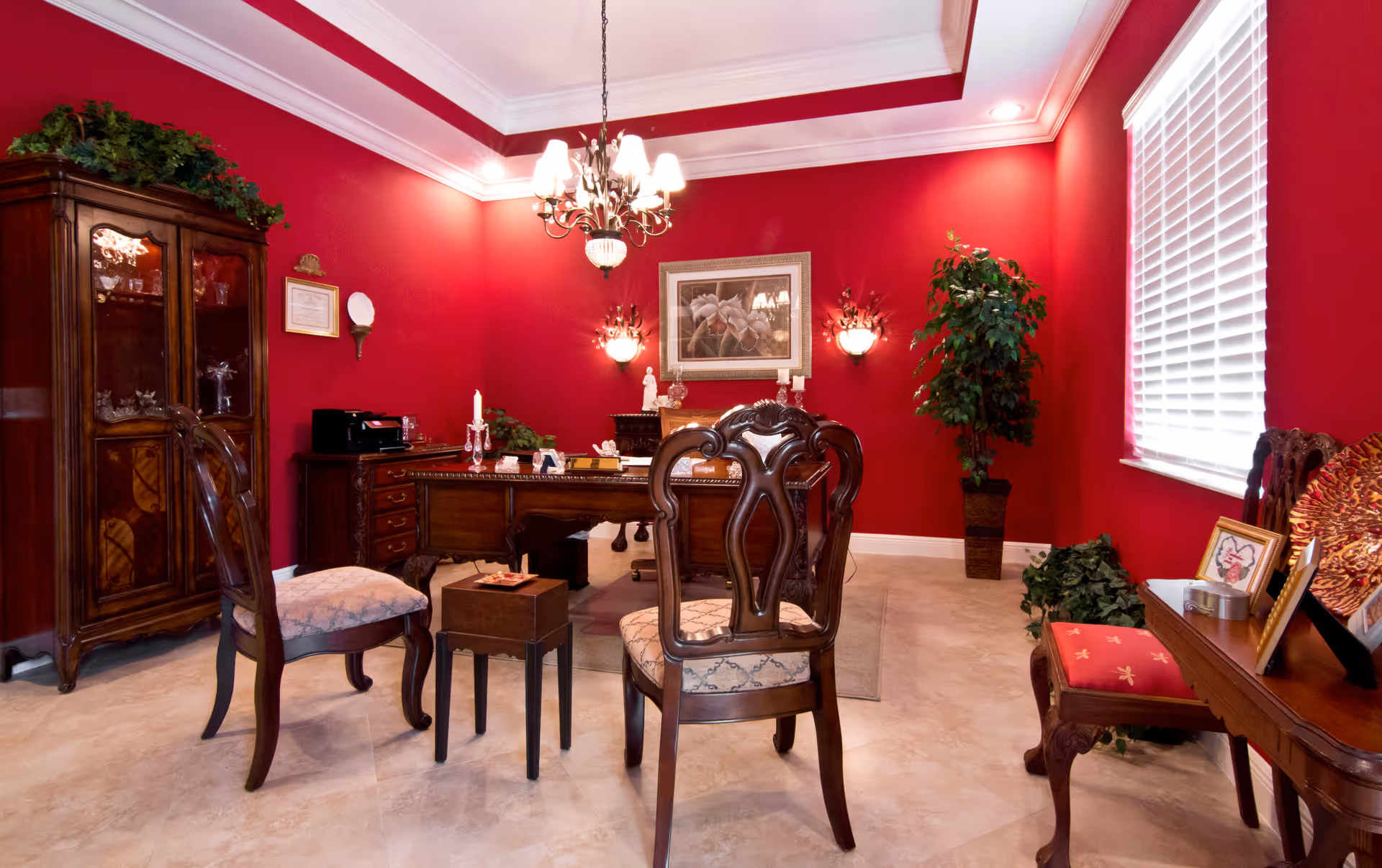 Red-walled, elegant office-like living area with dark wood furniture and chandelier.