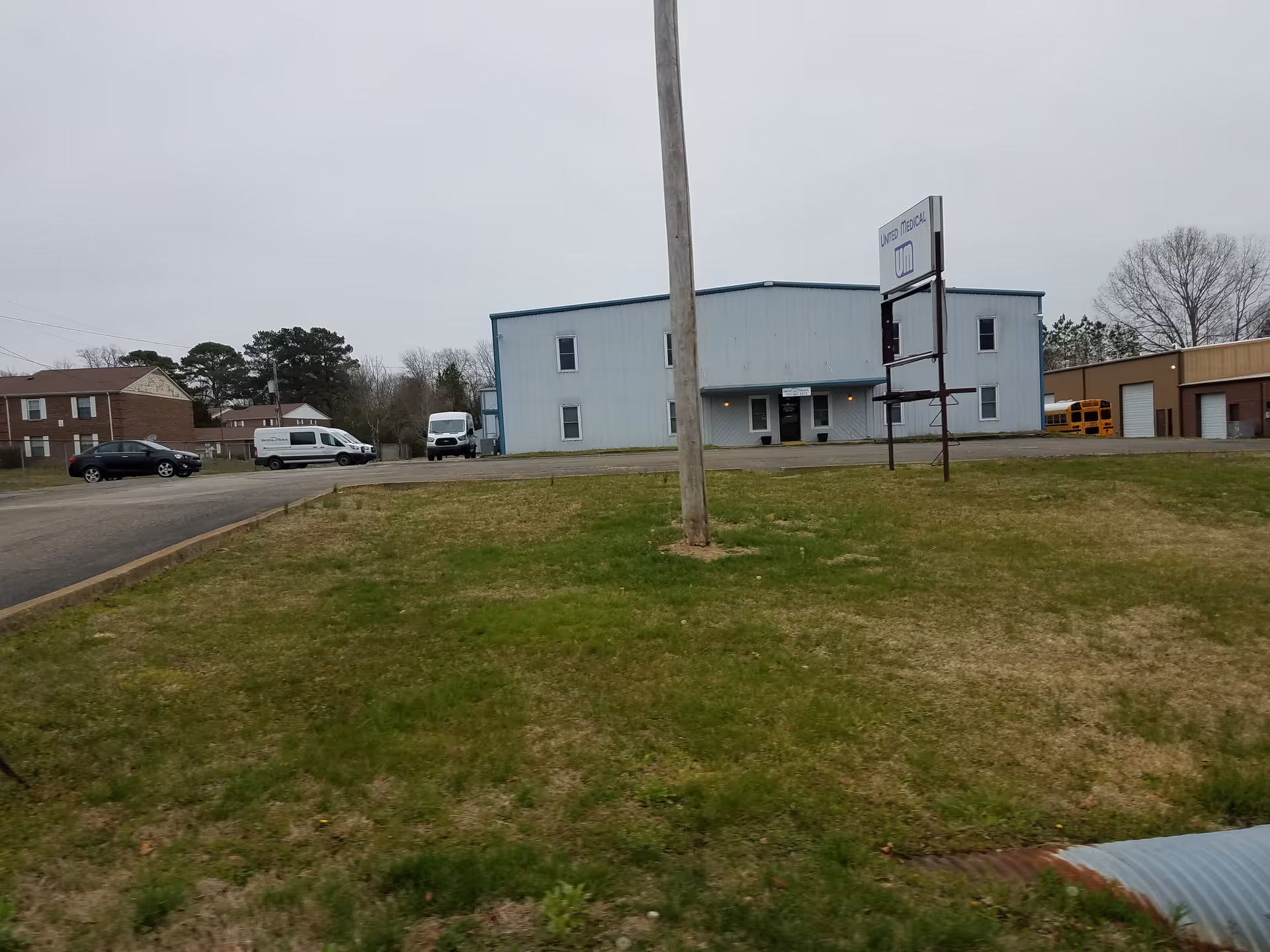 Blue medical facility building with sign, parked vehicles, and grassy foreground.