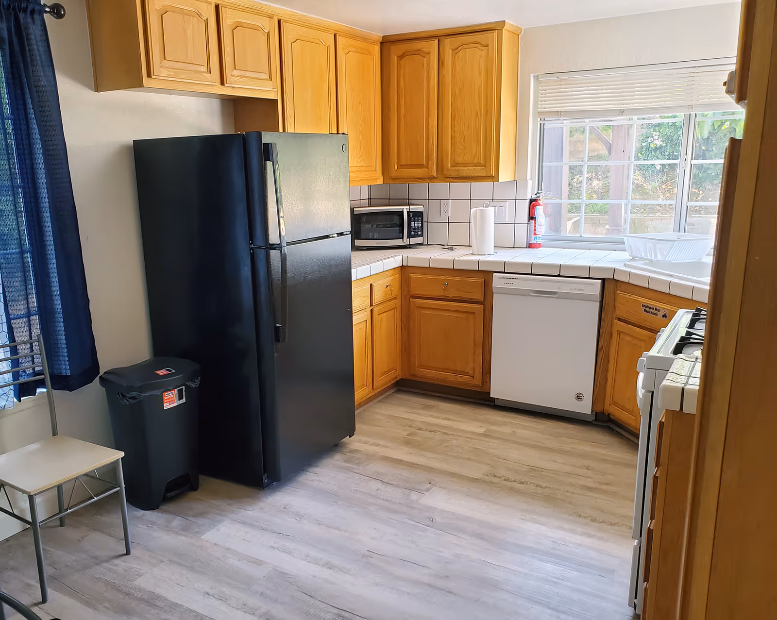 Kitchen area with wooden cabinets, fridge, microwave, stove, dishwasher, and a window.
