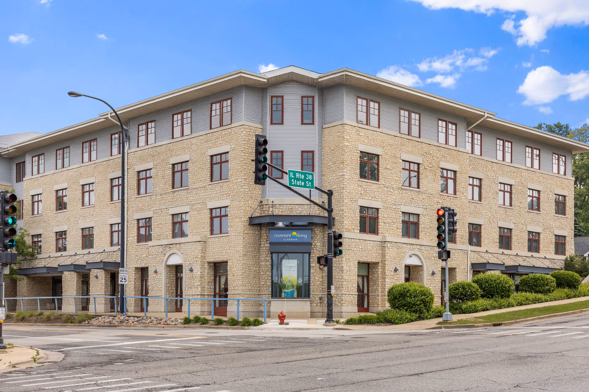 Three-story stone-and-siding senior living building on a street corner with traffic signals.