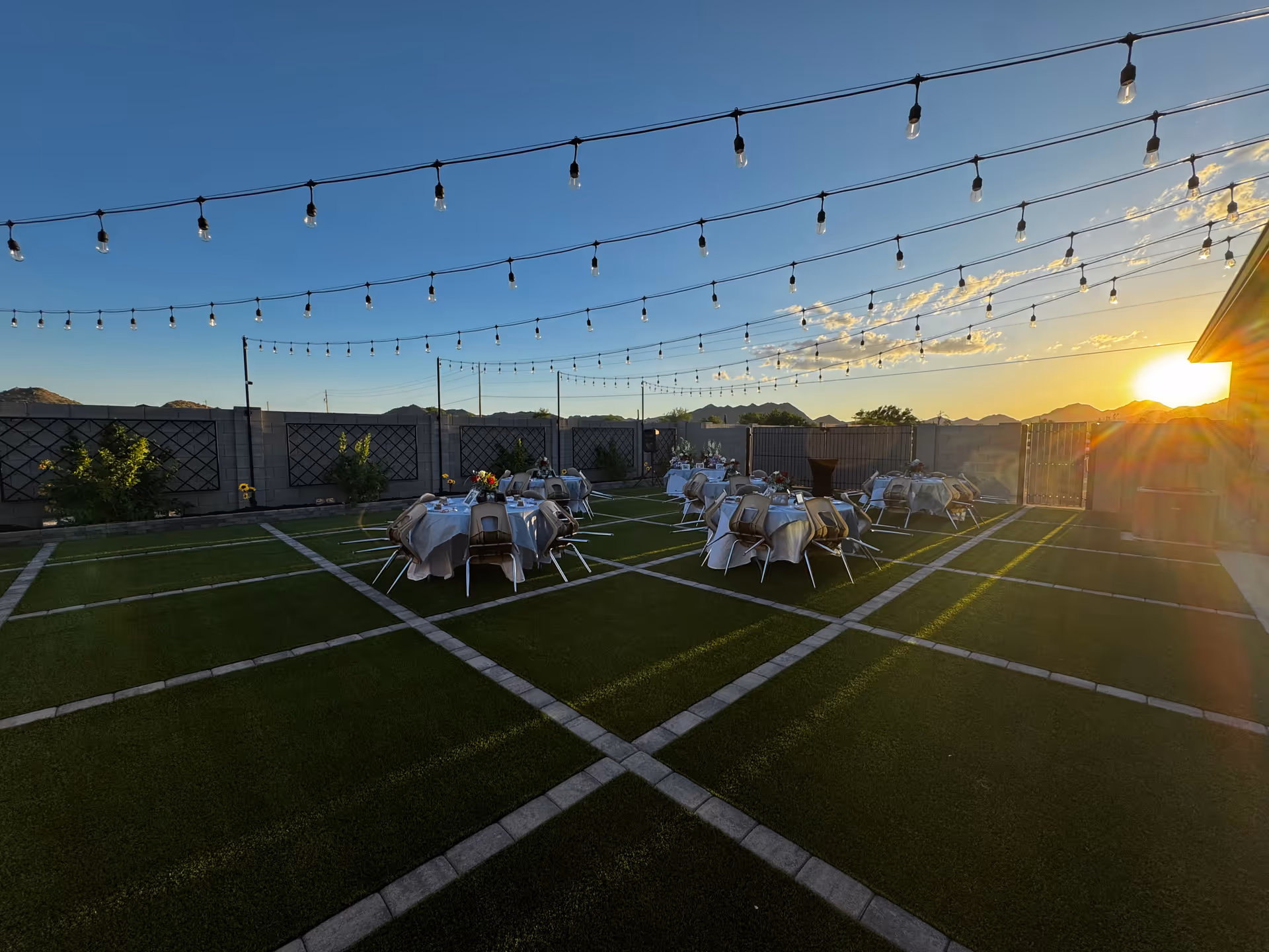 Outdoor terrace with string lights, arranged tables, and sunset glow.