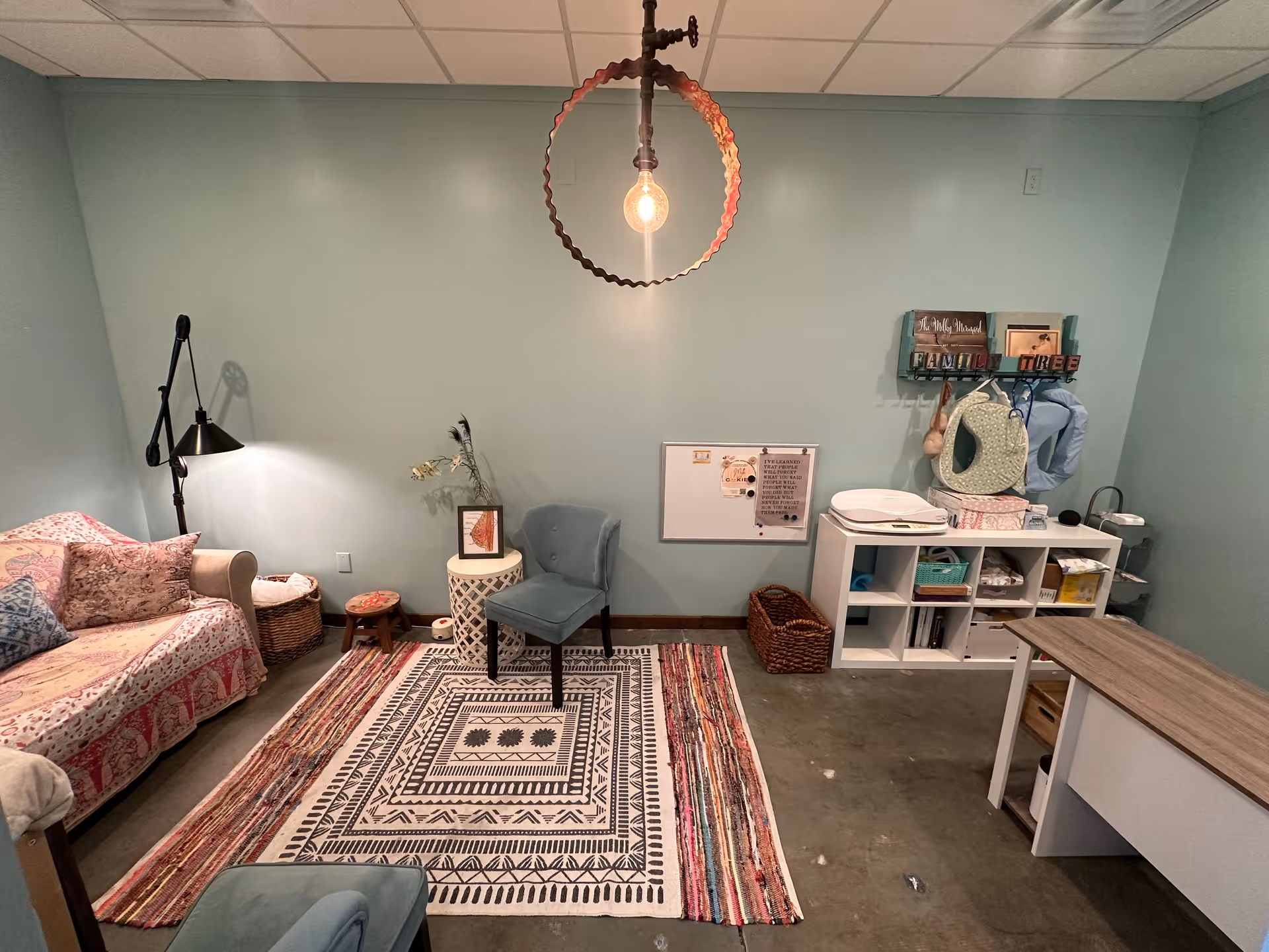 A cozy living room with teal walls, a sofa, chair, rug, and storage on the right.