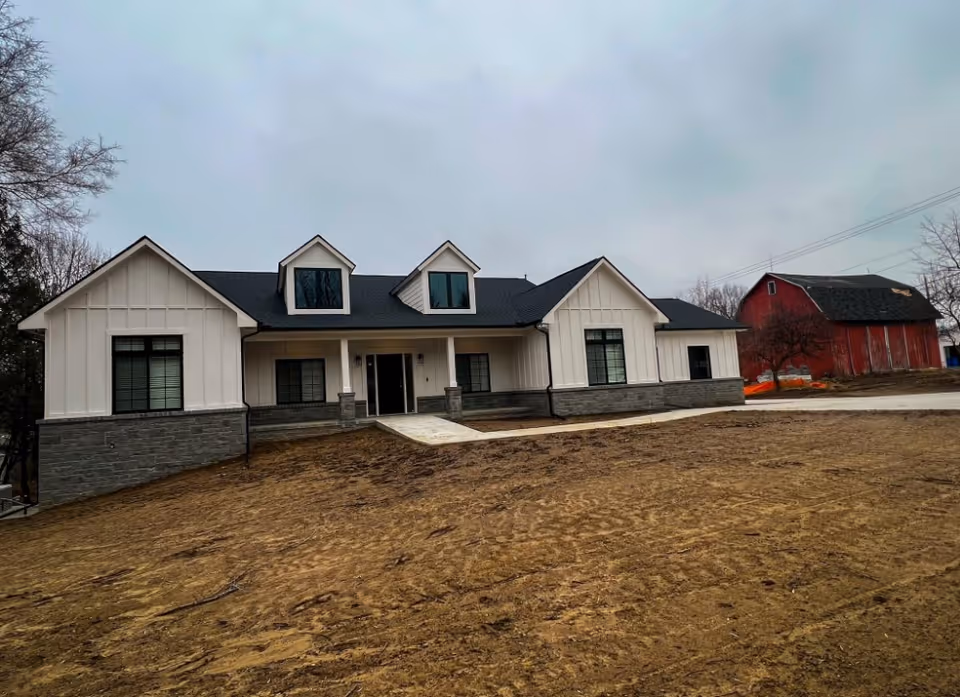 Front exterior of The Barns Senior Living with white siding, stone base, and dormers.