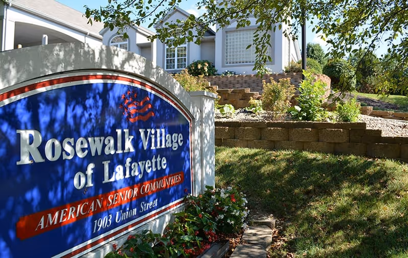 Entrance sign reading 'Rosewalk Village of Lafayette' in front of landscaped grounds and the facility building.