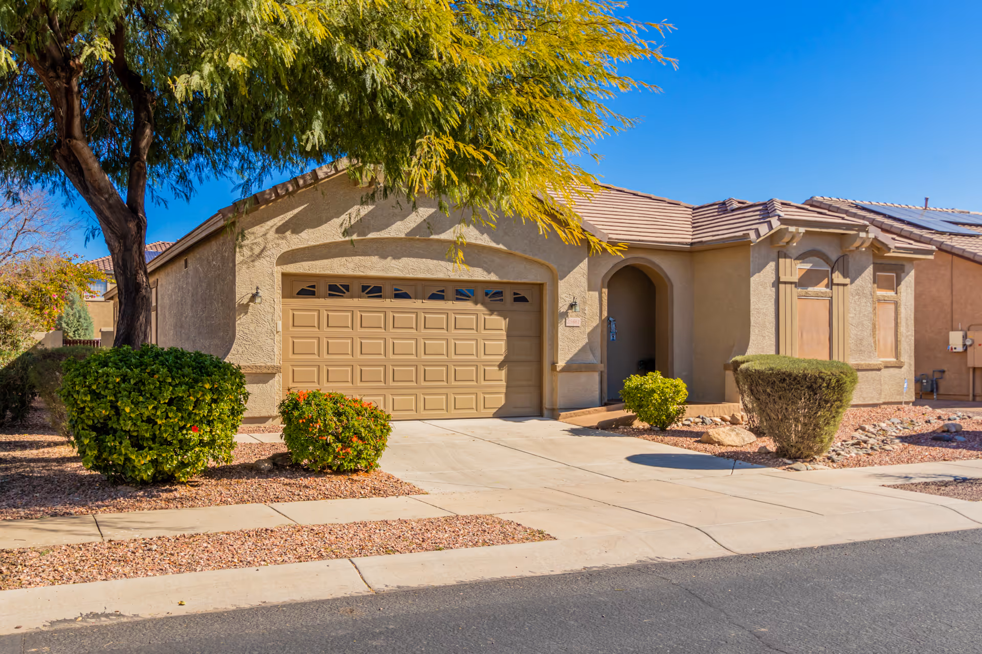 Beige stucco assisted living home exterior with arched entry, two-car garage, and desert landscaping.