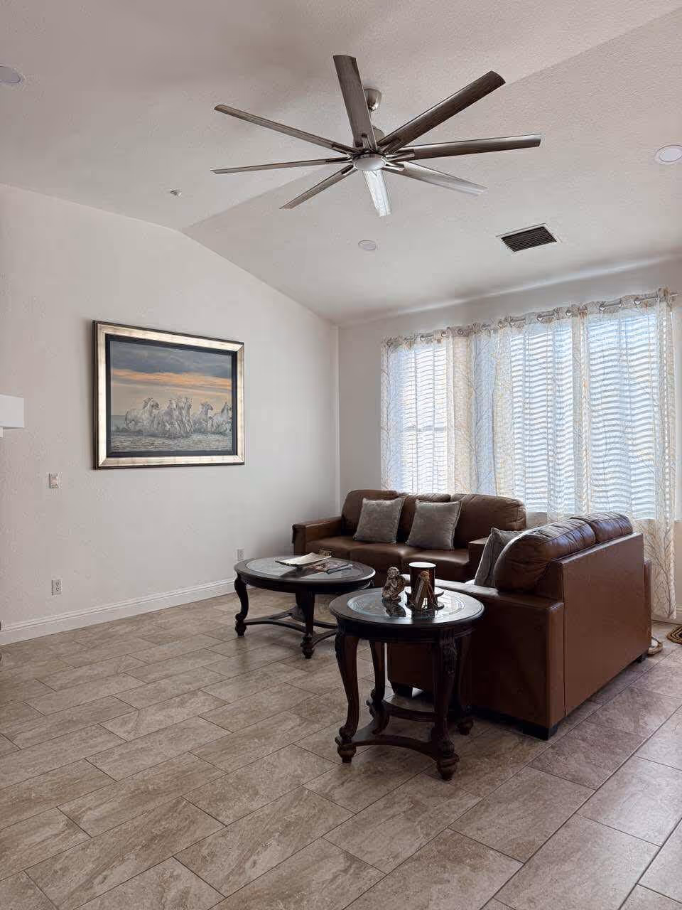 Bright living room with brown leather sofas, coffee tables, artwork, and large window.