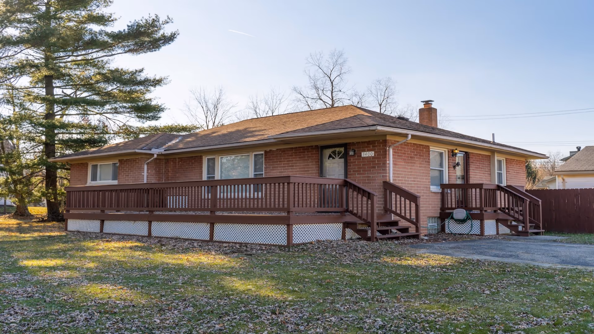 Single-story brick ranch house with a wraparound wooden porch and front steps on a grassy lot.