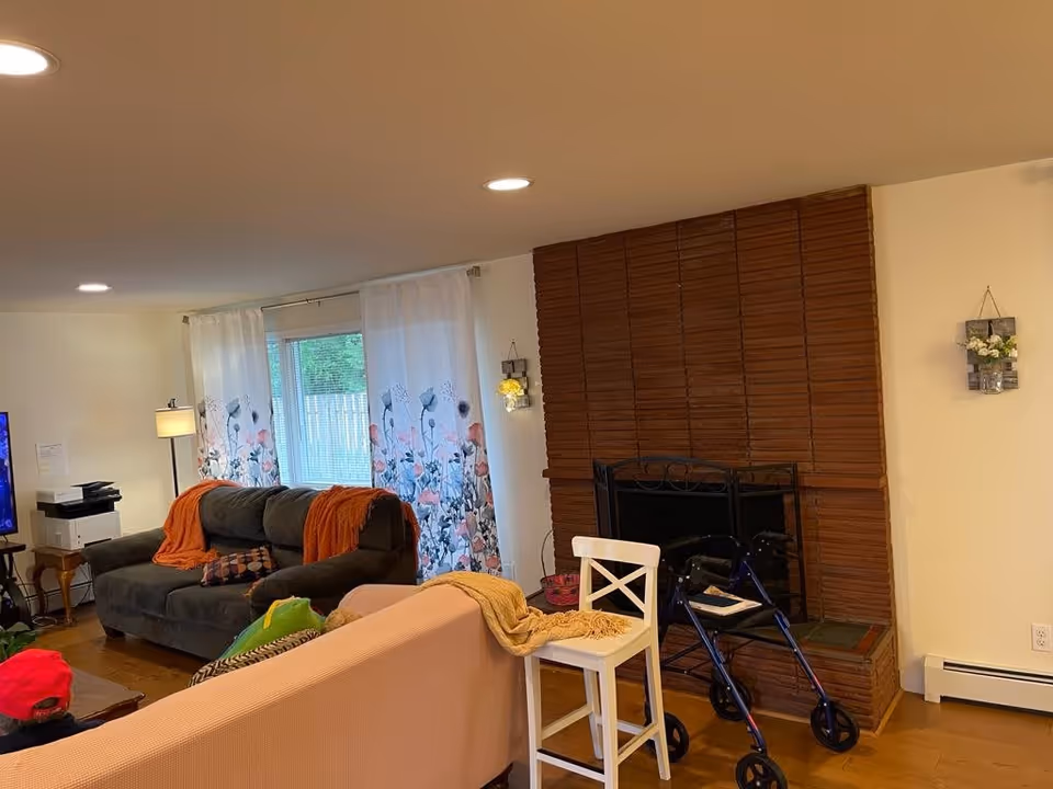 Cozy living room with sofas, floral curtains, a brick fireplace, TV, and a walker near a chair.