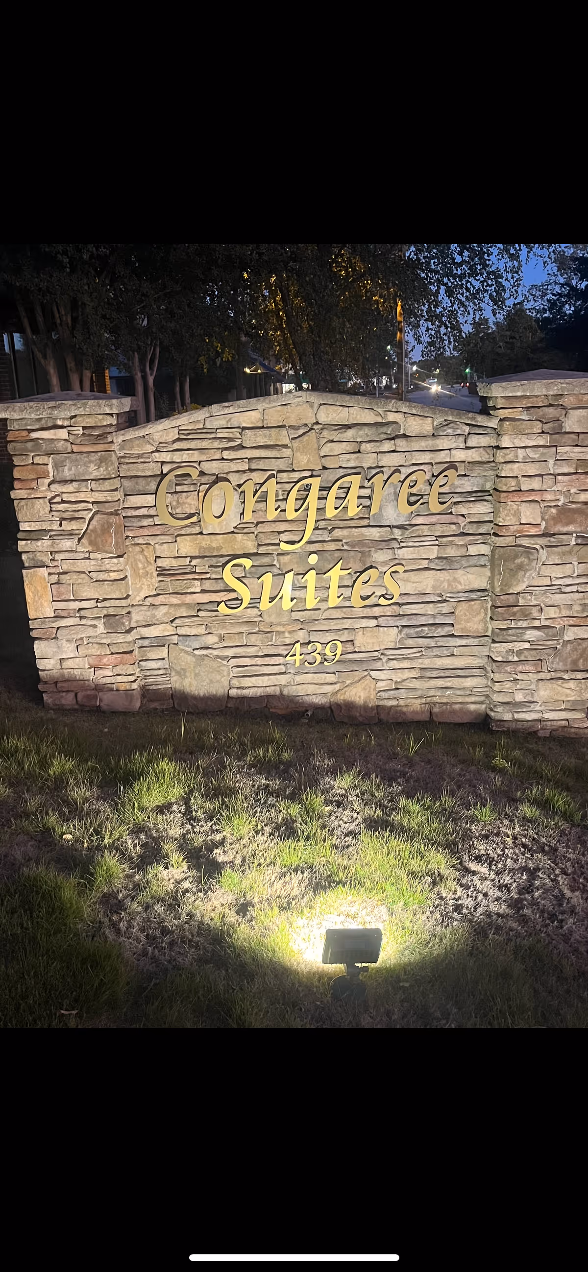 Stone entrance sign reading Congaree Suites illuminated at night.