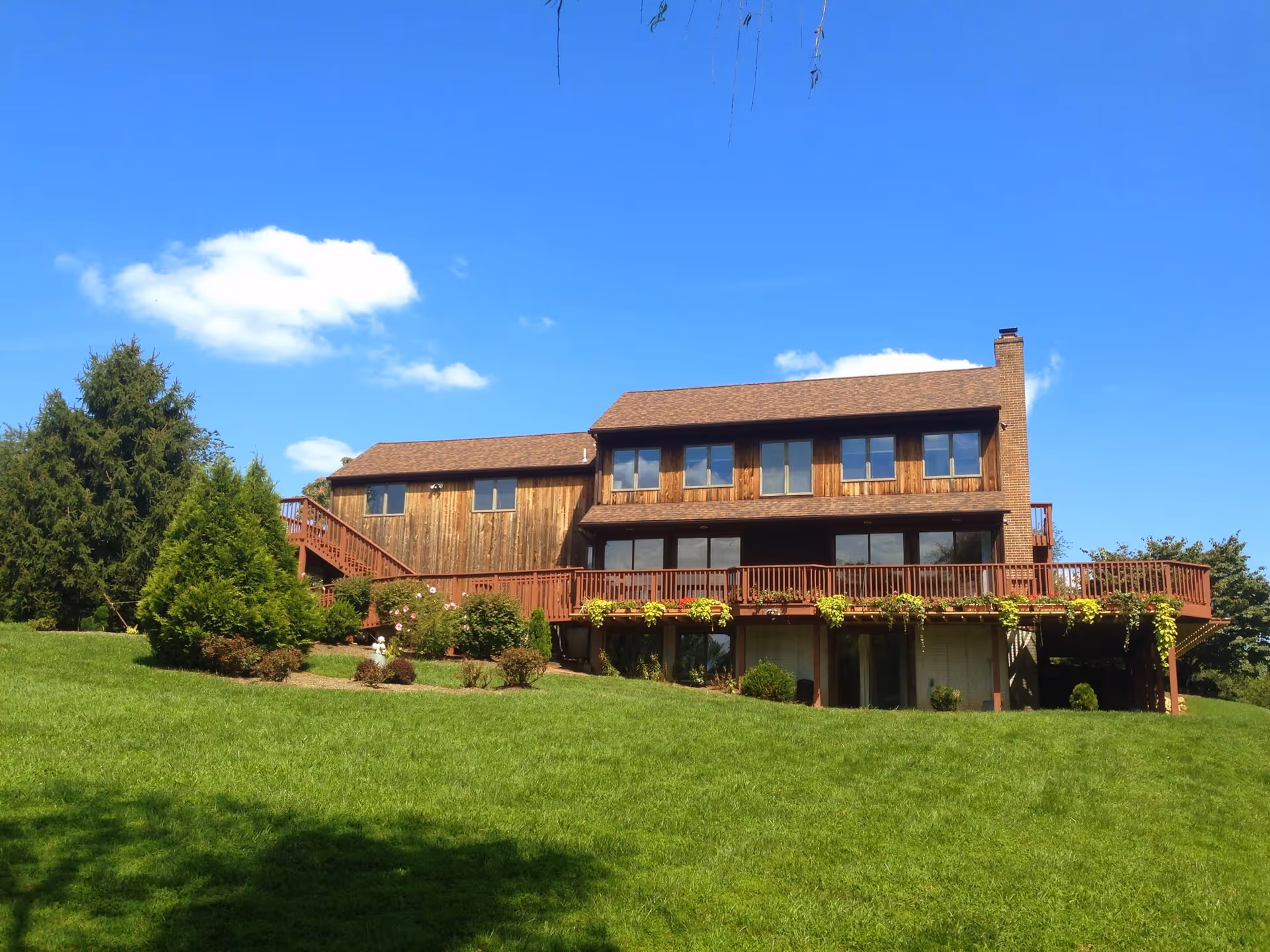 Two-story wooden senior living facility with expansive deck, green lawn, and clear blue sky.