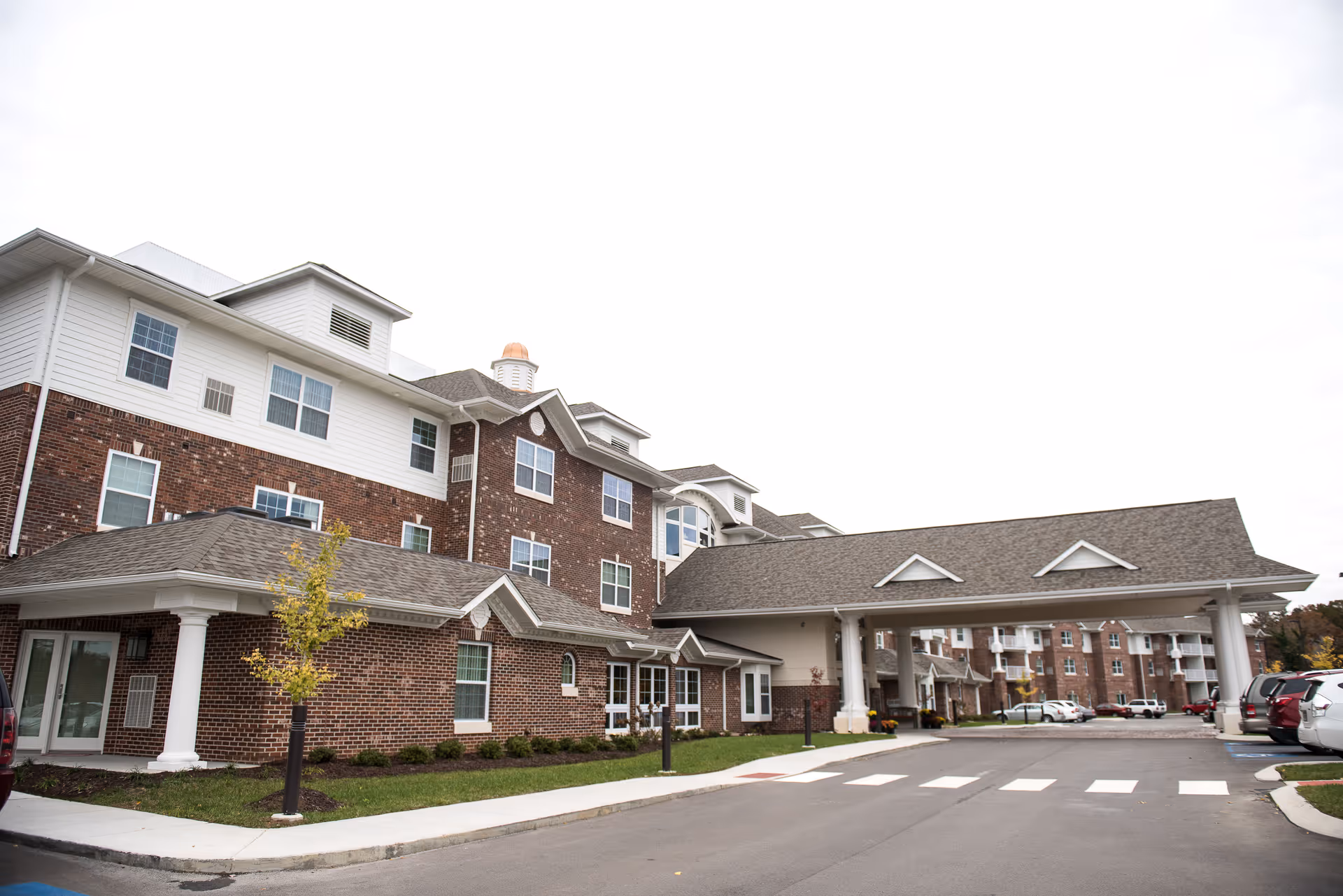 Exterior view of Ashwood Square Retirement Community with brick building, covered entrance, and parked cars.