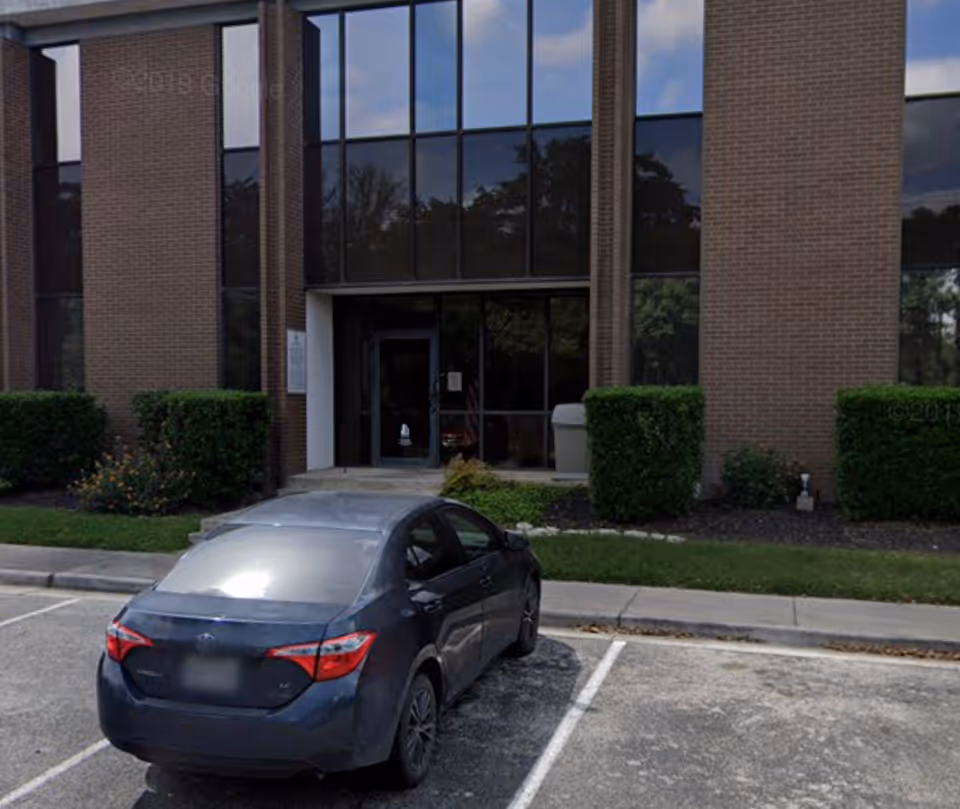 Exterior view of a brick facility entrance with large glass windows and a parked car.