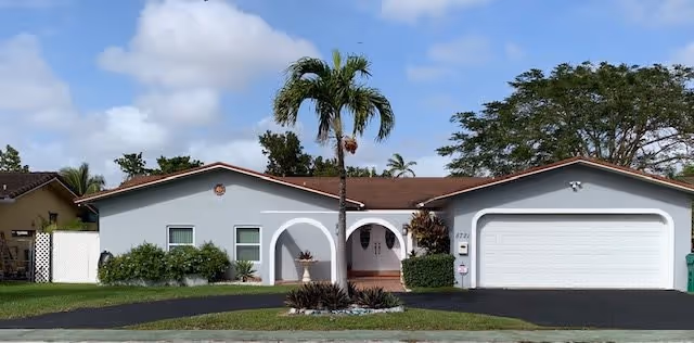 Single-story white ranch-style house with an arched front porch, attached two-car garage, palm tree and front lawn.