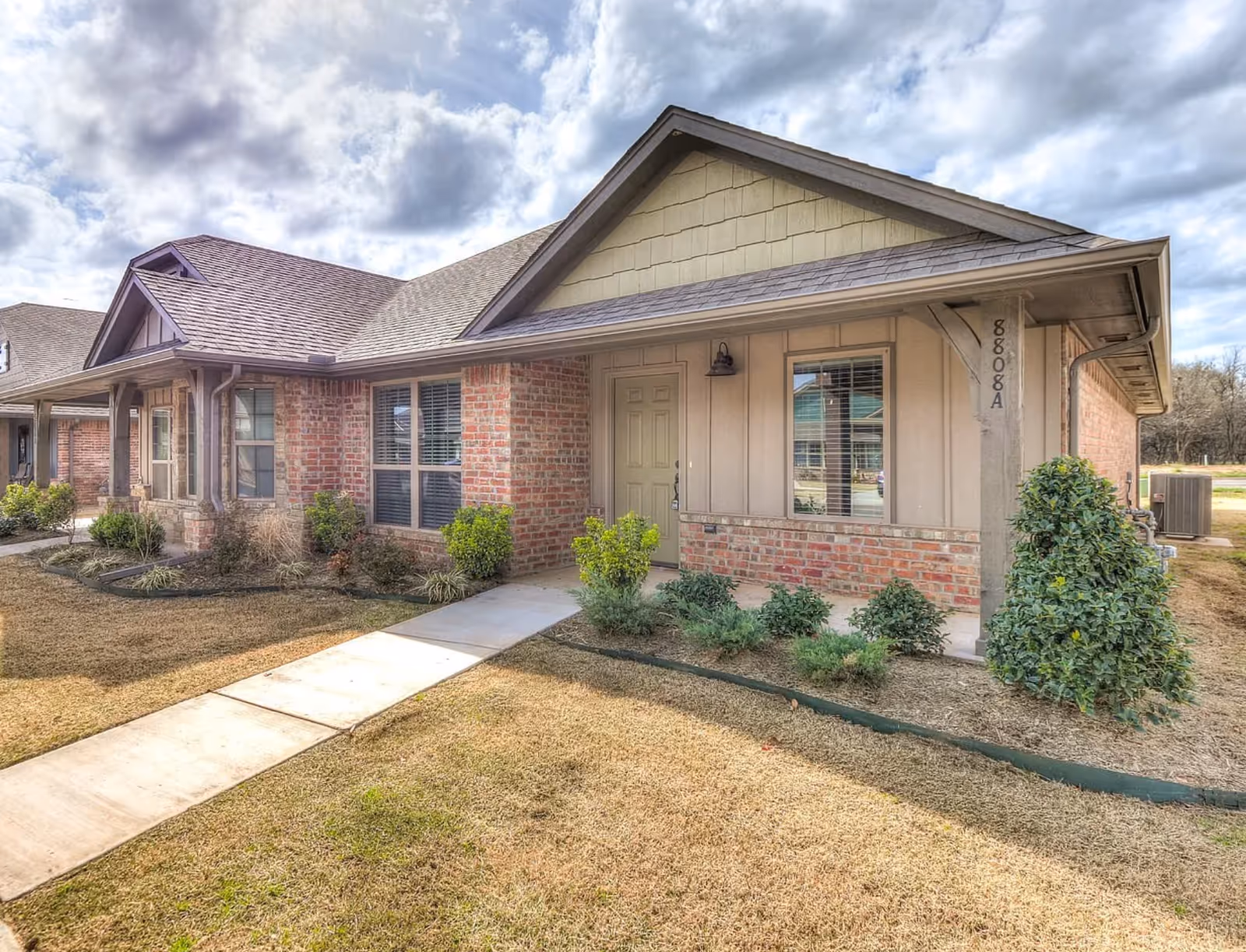 Single-story senior living facility front exterior with walkway, shrubs, and a pitched roof.