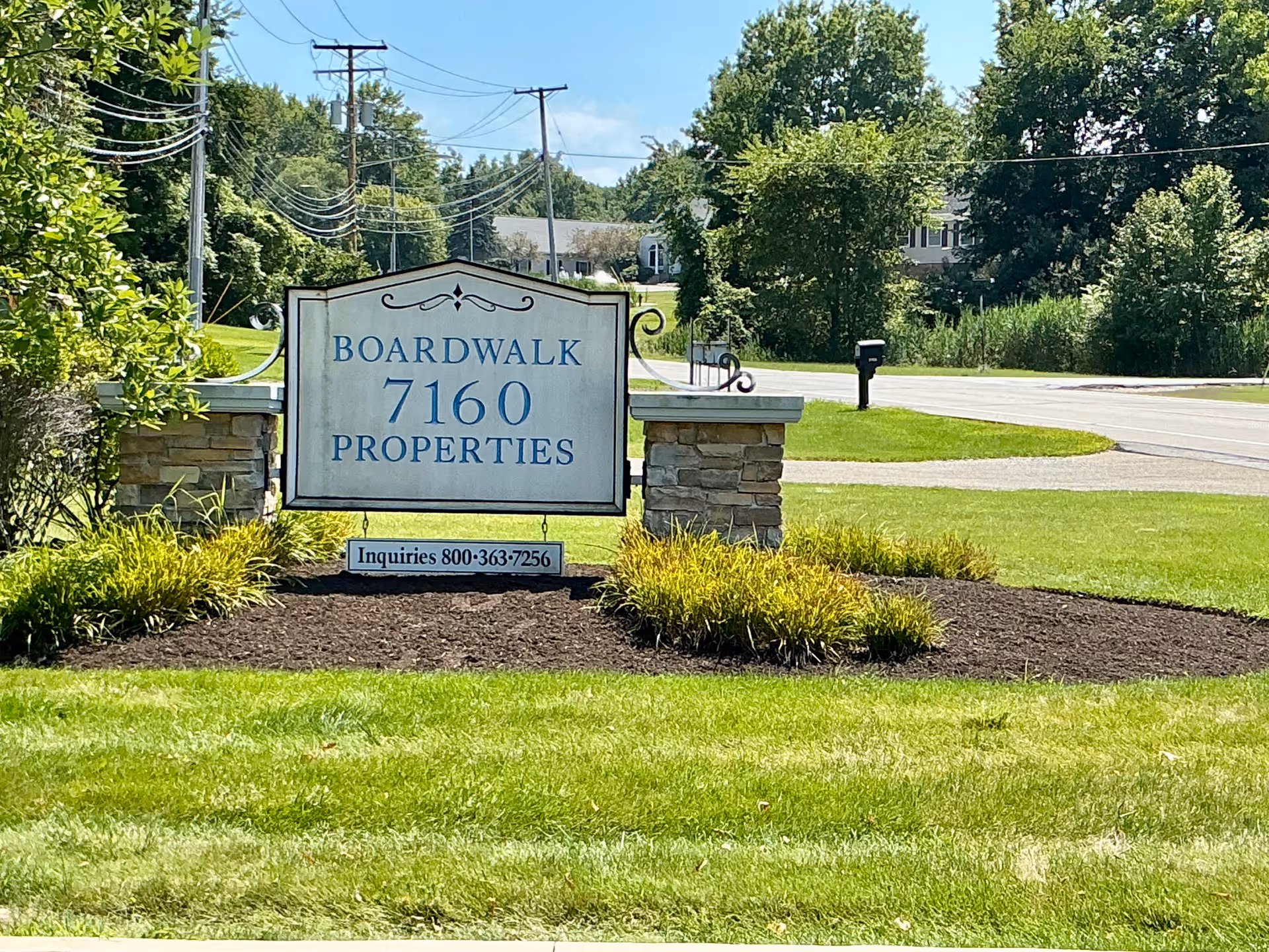 Outdoor sign reading Boardwalk Properties 7160 on a landscaped lawn with trees.