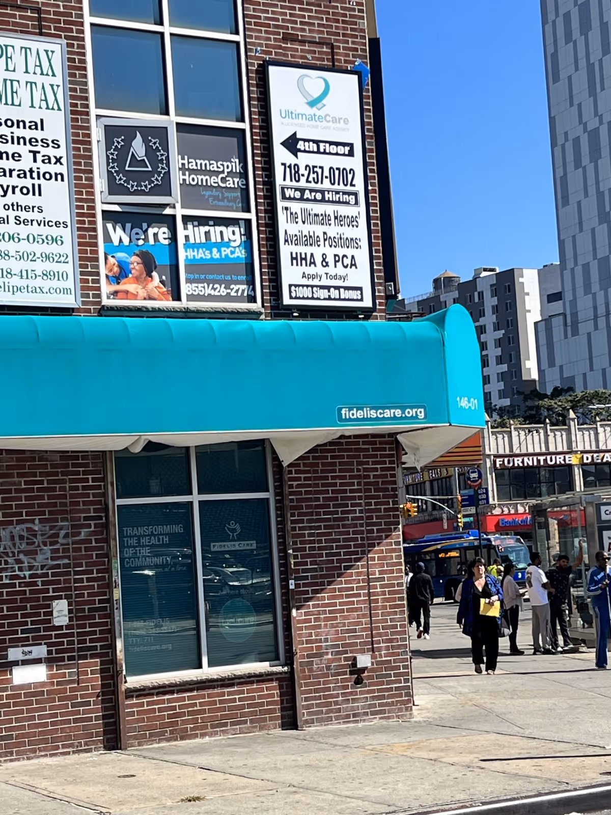 Brick storefront with teal awning; signs advertise Ultimate Care NY and hiring.