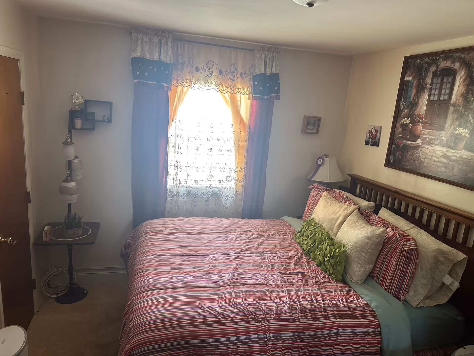Cozy bedroom featuring a striped bed, window with curtains, and wall art.